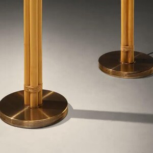 May include: Two bamboo floor lamps with round, brass-colored bases. The bamboo poles are bundled together and secured with woven material. The lamps are on a neutral background, casting shadows.