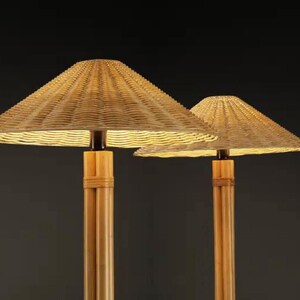 May include: Two lamps with woven, conical shades and bamboo-style bases. The shades are a light tan color, and the bases are a natural wood tone. The lamps are lit from within, casting a warm glow. The background is a dark gray.