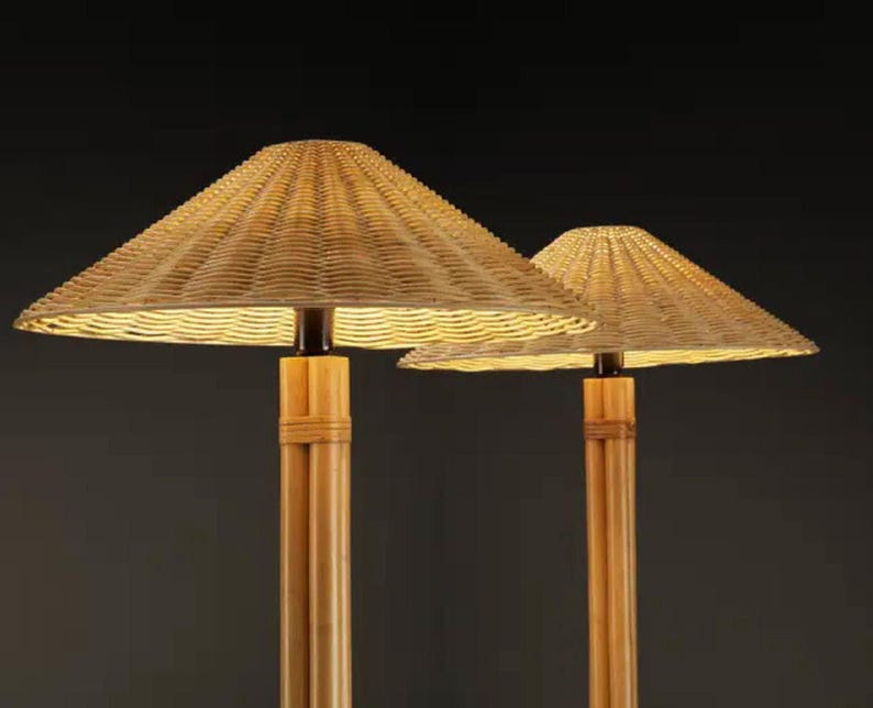 May include: Two lamps with woven, conical shades and bamboo-style bases. The shades are a light tan color, and the bases are a natural wood tone. The lamps are lit from within, casting a warm glow. The background is a dark gray.