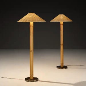 May include: Two bamboo floor lamps with woven shades. The lamps have a natural bamboo pole and a round, dark metal base. The shades are a light tan color and are angled. The lamps are lit, casting a warm glow.
