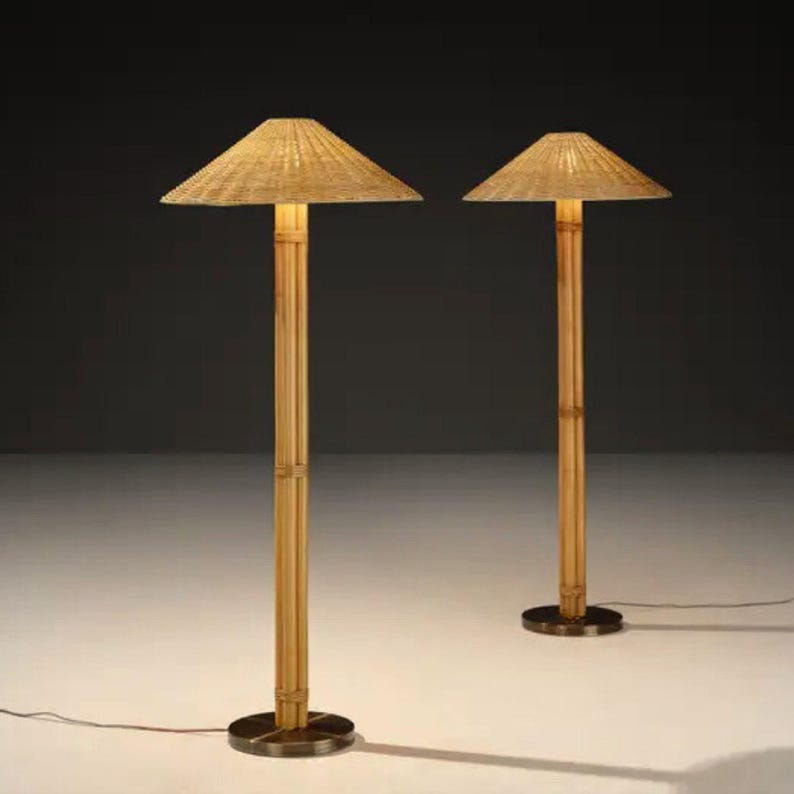 May include: Two bamboo floor lamps with woven shades. The lamps have a natural bamboo pole and a round, dark metal base. The shades are a light tan color and are angled. The lamps are lit, casting a warm glow.