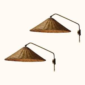 Puede incluir: Dos lámparas de pared con pantallas cónicas tejidas. Las pantallas son de color marrón dorado cálido, y los brazos y herrajes de montaje son de bronce oscuro. Las lámparas tienen un diseño minimalista, ideal para añadir un toque de elegancia rústica.