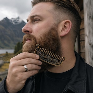 May include: A bronze-toned beard comb shaped like a Viking longship. The comb features a dragon head at the prow, a curved hull with a series of circular shield motifs along the side, and a row of vertical teeth for grooming facial hair.