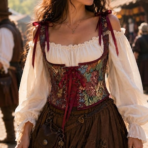 May include: A corset top featuring a multi-colored floral tapestry pattern with a front lace-up closure and dark red ribbon shoulder ties, worn over a cream-colored off-the-shoulder blouse with long sleeves and a brown skirt with a small pouch.