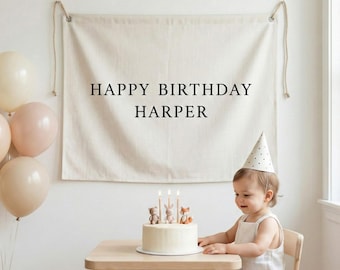May include: A birthday scene with a banner that reads "HAPPY BIRTHDAY HARPER." A small child wearing a party hat sits at a wooden table with a cake topped with candles and animal figurines. Balloons in neutral tones are in the background.