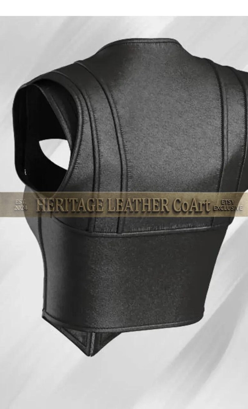 Puede incluir: Un chaleco negro sin mangas con paneles cosidos verticales y un dobladillo en punta. La prenda muestra el texto "EST. 2024 HERITAGE LEATHER CoArt ETSY EXCLUSIVE" en la parte central. El dise&ntilde;o incluye aberturas anchas para los brazos y un corte estructurado.