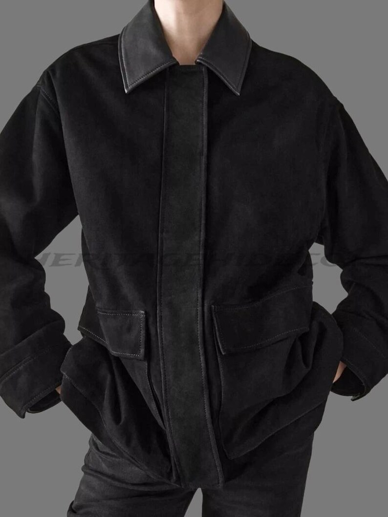 May include: A black jacket with a leather collar and accents. The jacket has two large front pockets and a vertical leather strip down the center. The sleeves are cuffed, and the jacket appears to be made of a soft material.