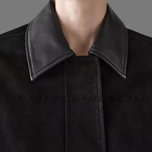 May include: Close-up of a black jacket with a contrasting black leather collar. The jacket has a classic design with a tailored fit. The collar is a sharp, pointed style. The text "HERITAGEHINECO1" is visible on the jacket.