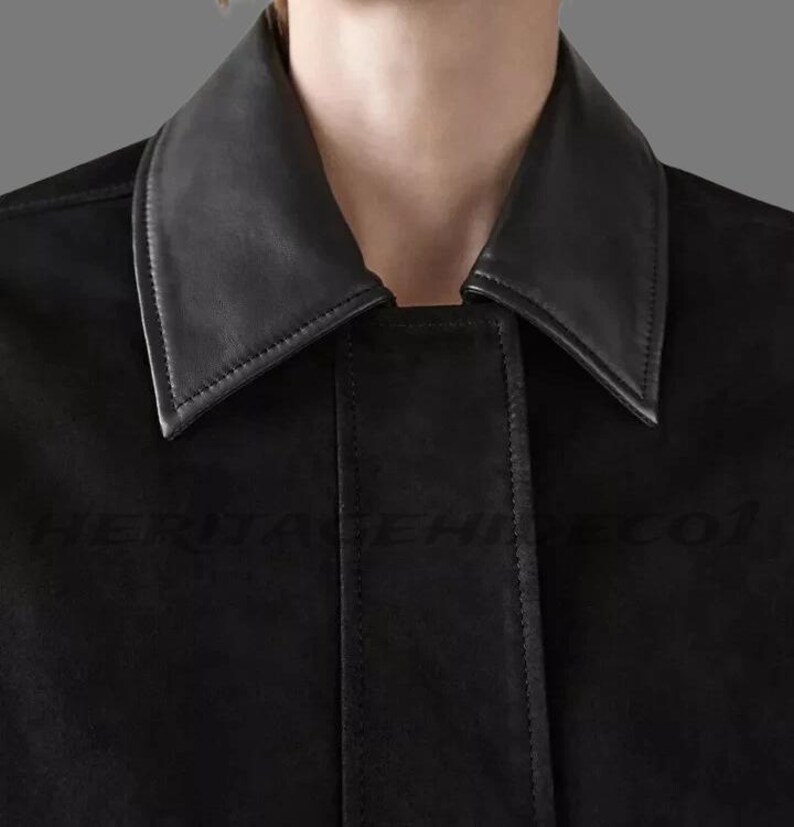 May include: Close-up of a black jacket with a contrasting black leather collar. The jacket has a classic design with a tailored fit. The collar is a sharp, pointed style. The text "HERITAGEHINECO1" is visible on the jacket.