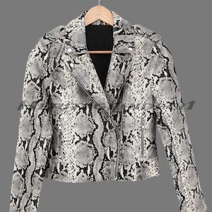 May include: A cropped biker jacket with a snakeskin pattern in black, white, and grey. The jacket has a notched collar, an asymmetrical zip, and zipped pockets. It hangs on a wooden hanger against a grey background.