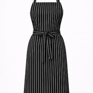 Puede incluir: Delantal a rayas blancas y negras con correa ajustable para el cuello y cinturón para atar. El delantal presenta rayas blancas verticales sobre un fondo negro. El cinturón está atado con un lazo. Adecuado para cocinar o manualidades.