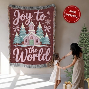 May include: A burgundy woven throw blanket with the words "Joy to the World" and a church graphic. The blanket features a fringed edge and a Christmas theme. The image also shows a mother and child.