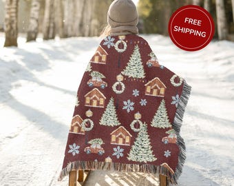 May include: A burgundy Christmas-themed throw blanket with a repeating pattern of houses, Christmas trees, wreaths, snowflakes, and cars carrying trees. The blanket has a fringed edge and is being used as a sled cover.