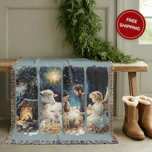 May include: A woven throw blanket with a religious scene depicting a nativity scene. The blanket features a light blue background with a detailed illustration of a stable, sheep, and figures. The blanket has a fringed edge.