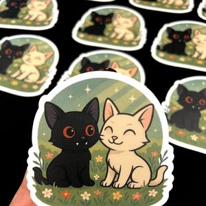 May include: A collection of stickers featuring a black cat and a cream-colored cat sitting together in a field of flowers. The cats have large eyes and are smiling. The background is a light green with stars.