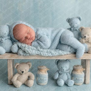 Puede incluir: Un bebé recién nacido durmiendo, vestido con un conjunto y una capucha de punto azul claro, descansando sobre un pequeño banco de madera. Varios osos de peluche en tonos azules y beige rodean al bebé, junto con dos pequeños tarros. El fondo es azul claro.