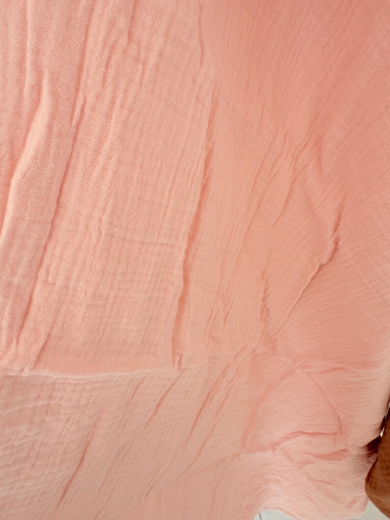 Puede incluir: Primer plano de una tela color melocot&oacute;n con una textura arrugada. El material tiene un aspecto suave y fluido, con pliegues visibles y sutiles variaciones de tono. La tela parece ligera, posiblemente una bufanda o chal.