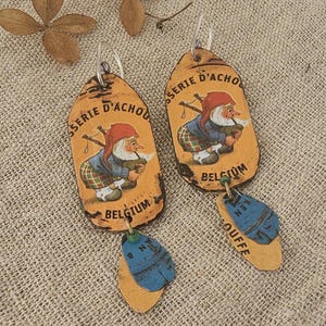 Pode incluir: Brincos artesanais com um design de estilo vintage. Os brincos têm um fundo amarelo com uma imagem de desenho animado de um gnomo com um chapéu vermelho e um cachimbo. Os brincos também têm um detalhe azul e amarelo na parte inferior.