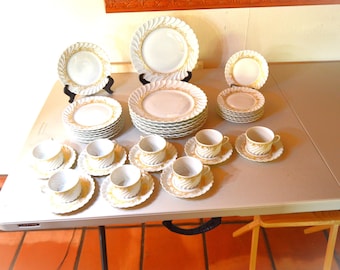 May include: A complete vintage dinnerware set featuring white plates, saucers, and teacups with a gold swirl design. The set includes various plate sizes and teacups with matching saucers, all arranged on a white table.