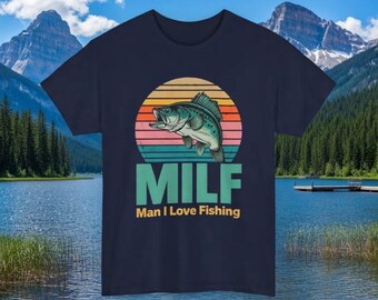 Puede incluir: Una camiseta azul marino de manga corta con un gráfico de un pez saltando frente a un círculo de atardecer retro. Debajo del pez, el texto MILF aparece en letras grandes, con las palabras Man I Love Fishing impresas debajo.