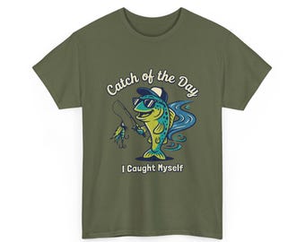 May include: Olive green t-shirt featuring a cartoon fish wearing sunglasses and a hat, holding a fishing rod. The text "Catch of the Day" and "I Caught Myself" are above and below the fish illustration.