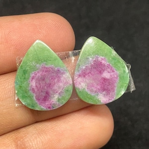 Może przedstawiać: Dwa kamienie szlachetne w kształcie łezki. Każdy kamień ma żywą zieloną warstwę zewnętrzną z centralną, nieregularną plamą w głębokim różu. Kamienie są trzymane razem przezroczystą taśmą, ukazując ich wypolerowane powierzchnie.