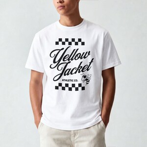 Pode incluir: Camiseta branca com o texto "Yellow Jacket ATHLETIC CO." em escrita preta e um desenho de abelha de desenho animado. O design é emoldurado por padrões quadriculados em preto e branco na parte superior e inferior.