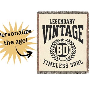 May include: Cream-colored throw blanket with black text that reads "LEGENDARY VINTAGE" above a circular design with the number "80" and the words "TIMELESS SOUL". The blanket has a fringed edge. A yellow starburst graphic with the words "Personalize the age!" is on the left.