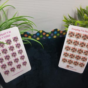 Può includere: Due fogli di adesivi con la scritta "Everyday I'm Hustling!!!" e illustrazioni di disegni floreali. Un foglio presenta fiori viola e l'altro fiori marroni. Gli adesivi sono su sfondo bianco.