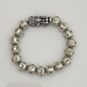 May include: Silver beaded bracelet featuring a detailed centerpiece and round beads with etched symbols. The bracelet is made of silver and has a polished finish. The beads are approximately 0.5 inches in diameter.