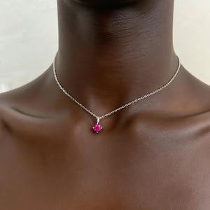 May include: A silver necklace with a small, round, bright pink gemstone pendant. The chain is delicate and sits around the neck. The gemstone is the focal point, catching the light and adding a pop of color.