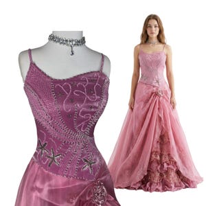 May include: A floor-length dusty rose gown featuring a fitted bodice with intricate beadwork, star-shaped embellishments, and thin spaghetti straps. The skirt has a layered, ruffled design with a fabric rose accent at the waist. A silver choker is included.