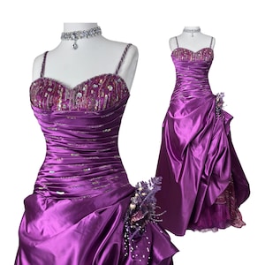 May include: A formal purple gown with a sweetheart neckline and spaghetti straps. The bodice is embellished with sequins and beads. The skirt features a draped design with a floral accent. A matching beaded choker necklace is included.