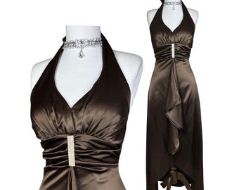 Puede incluir: Vestido halter de satén marrón con escote en V y dobladillo asimétrico. El vestido presenta un corpiño fruncido con un adorno vertical de pedrería y perlas. También se incluye un collar gargantilla plateado con un colgante.