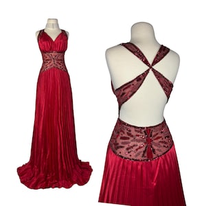 Könnte beinhalten: Ein rotes Abendkleid mit einem plissierten Rock und einem V-Ausschnitt-Oberteil. Das Oberteil und der Rücken weisen aufwendige Pailletten- und Perlenverzierungen auf. Das Kleid wird auf einer Schaufensterpuppe präsentiert.