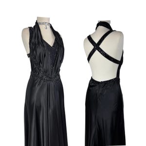 May include: A black halter dress with a beaded neckline and waist, displayed on a mannequin. The dress has a low back with beaded straps. The fabric has a satin sheen. A silver necklace is around the mannequin's neck.
