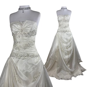 Peut inclure: Une robe bustier ivoire avec un décolleté en cœur, un corsage froncé et une jupe ample en tissu superposé. La robe est ornée de perles argentées complexes et de cristaux transparents sur le corsage et la jupe, accompagnée d'un tour de cou assorti.