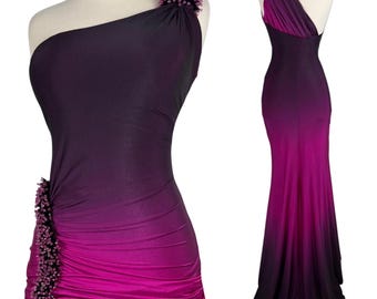 May include: A floor-length one-shoulder gown featuring a dark purple to magenta ombre gradient. The dress includes gathered fabric detailing at the waist and shoulder, accented with clusters of small dark beads on the shoulder and side.