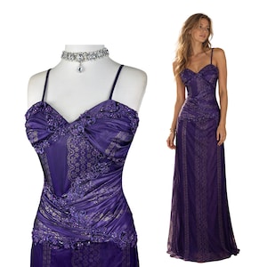May include: A floor-length purple gown featuring thin spaghetti straps, a sweetheart neckline, and intricate floral lace detailing. The bodice is adorned with gathered fabric and beadwork, while the skirt displays a vertical patterned design.