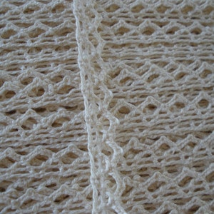 May include: Close-up of a white crocheted fabric with a diamond pattern. The fabric has a delicate, lacy texture.
