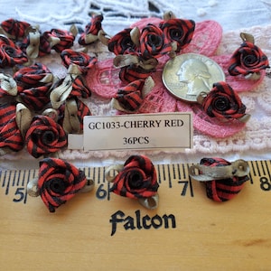 May include: A collection of small, fabric rose embellishments in cherry red and black stripes, with tan ribbon accents. The tag reads "GC1033-CHERRY RED 36PCS". A US quarter is included for size reference. The roses are on a pink lace background.