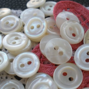 May include: A collection of white pearl buttons with two holes each. The buttons are arranged in a random pattern on a red and white fabric background.