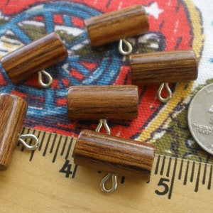 Può includere: Sei bottoni a scatto in legno marrone con anelli metallici. I bottoni sono disposti su una superficie di tessuto con un righello e una moneta da 25 centesimi.