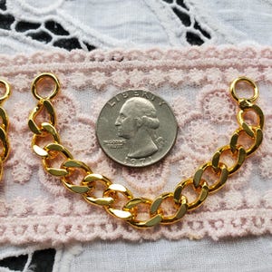 May include: Close-up of two gold-colored chain segments with a quarter coin for size comparison. The chains have a curb link design and are attached to small circular loops. The coin shows the profile of George Washington.