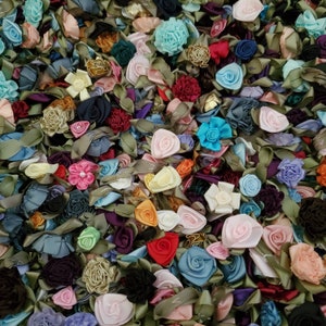 May include: A close-up of a variety of colorful fabric flowers. The flowers are made of satin ribbon and are arranged in a random pattern. The colors include red, blue, green, yellow, pink, and white.