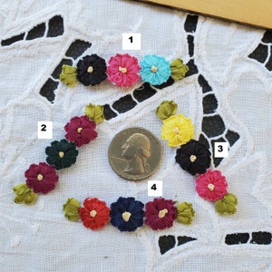 May include: Assortment of ten colorful fabric flowers with green leaves. The flowers are arranged in four rows, with a US quarter for scale.
