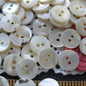 May include: A large pile of white, two-hole, round, mother-of-pearl buttons.