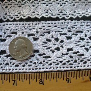 May include: White cotton lace trim with a delicate floral pattern. The lace is approximately 1 inch wide and is shown next to a ruler for scale.