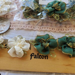 May include: Close-up of various craft supplies, including green and cream-colored fabric flowers and trim. The word "Falcon" is printed on a wooden ruler. Some items are packaged in clear plastic.