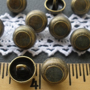 May include: A collection of 10 antique gold-toned metal buttons with a raised, circular design. The buttons have a smooth, slightly textured surface and a shiny finish.